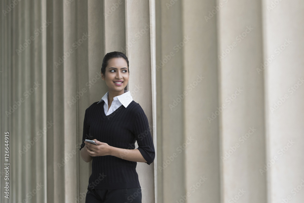 business woman holding mobile phone in front of columns business woman holding mobile phone in front of columns