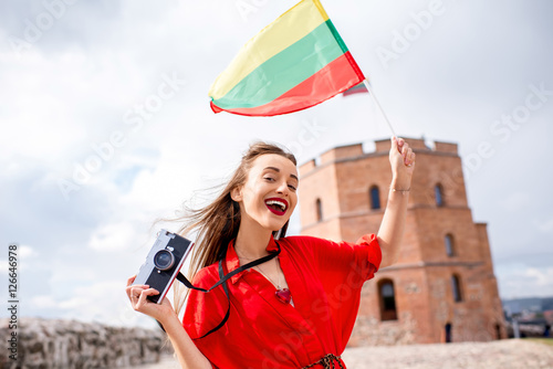 Portrait of a young female tourist with lithuanian flag in front of the famous old tower in Vilnius. Woman having great vacations in Lithuania