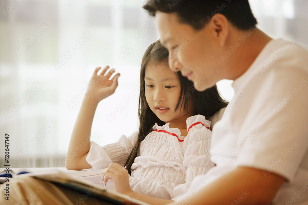 Father and daughter, sitting side by side, looking at book Father and daughter, sitting side by side, looking at book