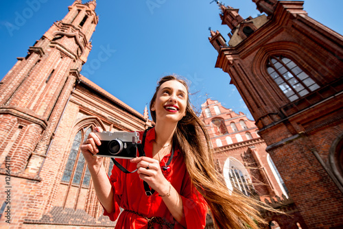 Young female tourist with photo camera standing in front of the famous gothic church in the old town of Vilnius. Woman having great vacations in Lithuania