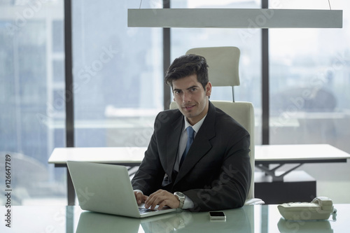 India, Businessman at desk looking up from over laptop