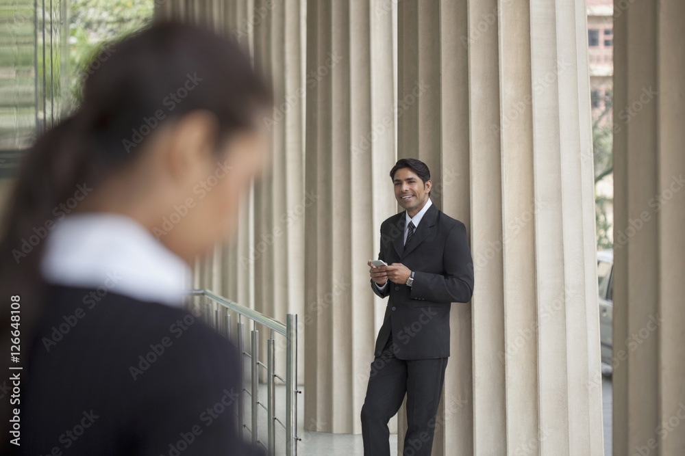India, Businessman using mobile phone looking up at colleague in distance India, Businessman using mobile phone looking up at colleague in distance