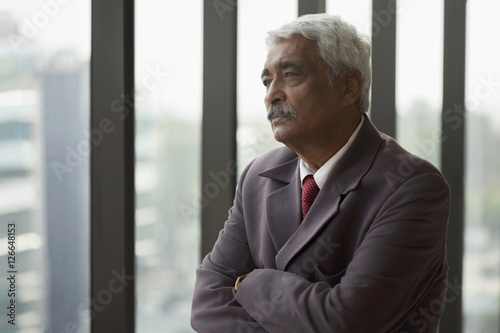 India, Portrait of senior businessman with arms folded looking through window