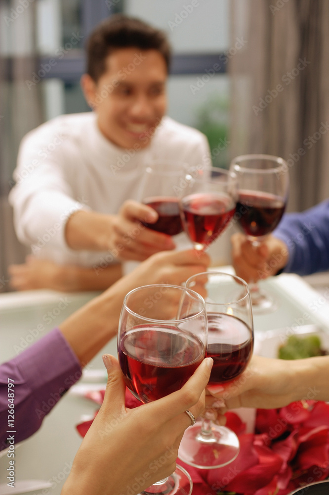 Friends toasting with wine glasses across dinner table