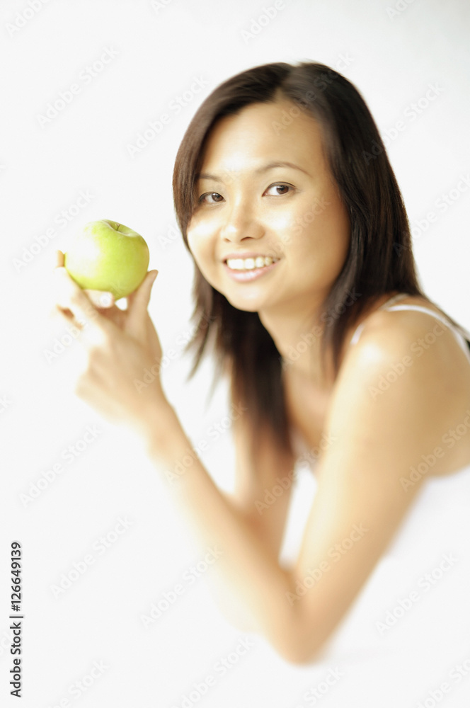 Young woman lying on floor, holding apple, smiling at camera Young woman lying on floor, holding apple, smiling at camera