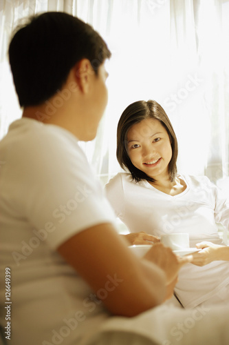 Couple having coffee, sitting on sofa, woman looking at camera