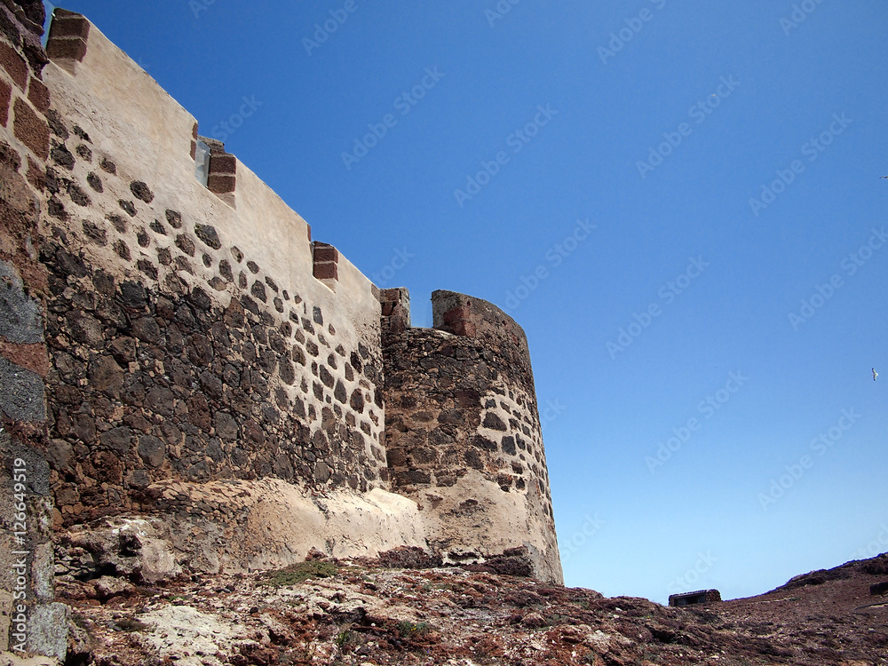 Medieval fortress wall on the hillside against the backdrop of deep blue sky. Teguise, Lanzarote, Canary Islands, Spain