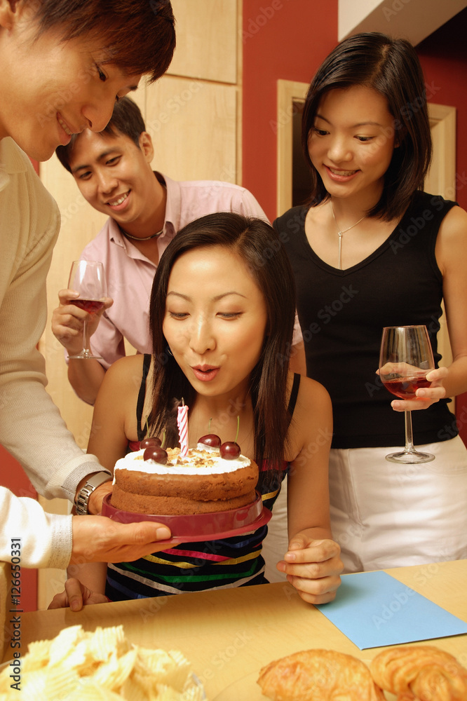 Woman blowing out candle on cake, surrounded by friends