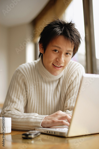 Photography Young man sitting at table with laptop, looking at camera