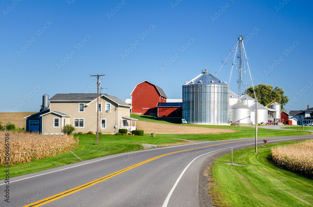 Farm with Silos and Red Barn along a Country Road under Clear Sky