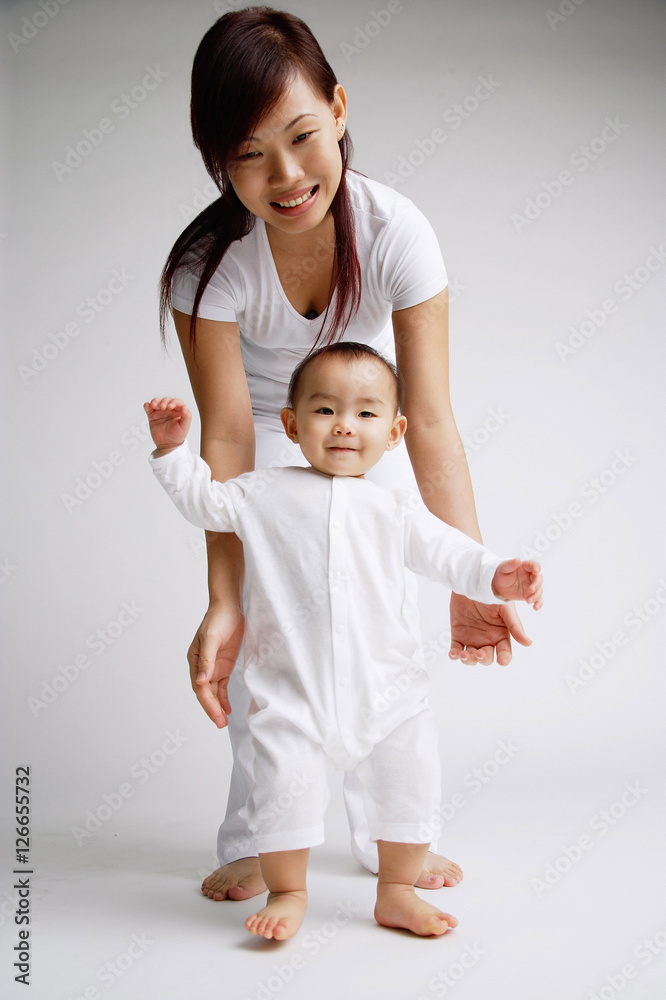 Baby girl standing, mother behind her, portrait Baby girl standing, mother behind her, portrait