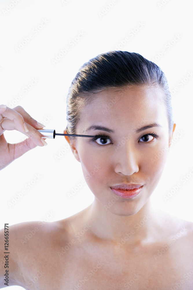 Fototapeta premium Woman holding mascara wand, looking at camera