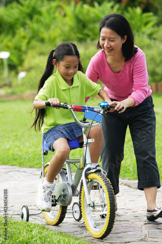 Young girl cycling, mother guiding her