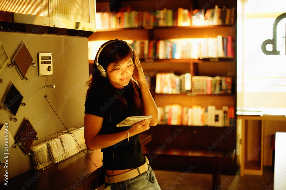 Young woman standing, listening to music, holding CD