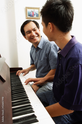 Father and son sitting at piano, looking at each other