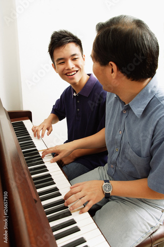 Father and son playing piano, side by side