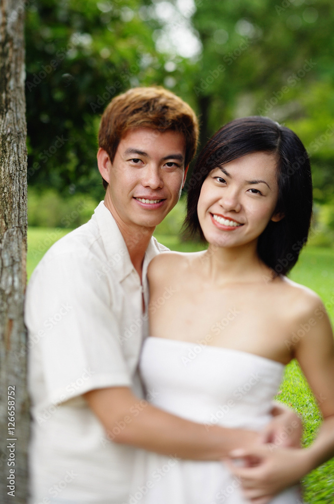 Couple leaning on tree, embracing, looking at camera Couple leaning on tree, embracing, looking at camera