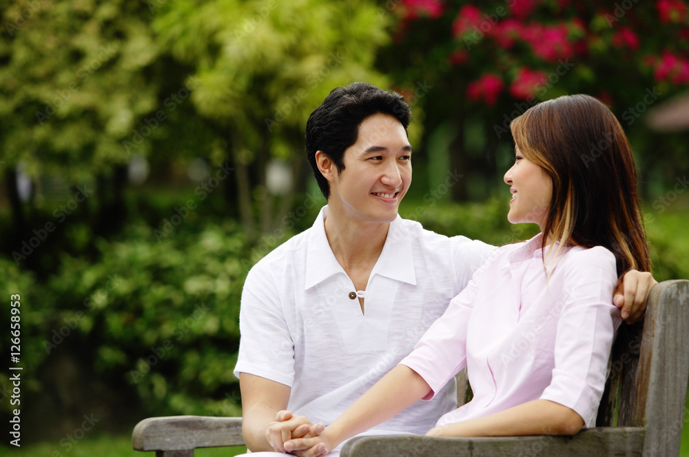 Couple sitting on park bench, holding hands, looking at each other