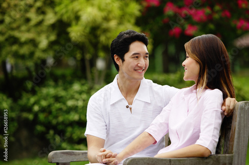 Obraz na płótnie Couple sitting on park bench, holding hands, looking at each other w salonie