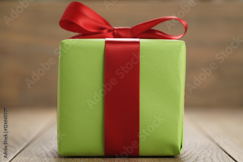 green paper gift box with classic red ribbon bow on wooden table