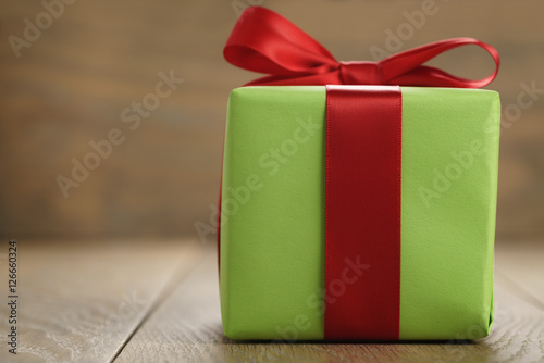 green paper gift box with classic red ribbon bow on wooden table