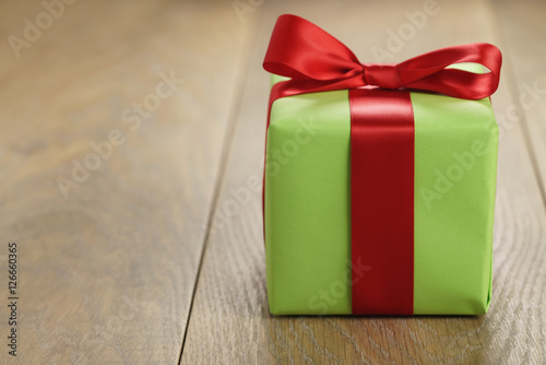 green paper gift box with classic red ribbon bow on wooden table