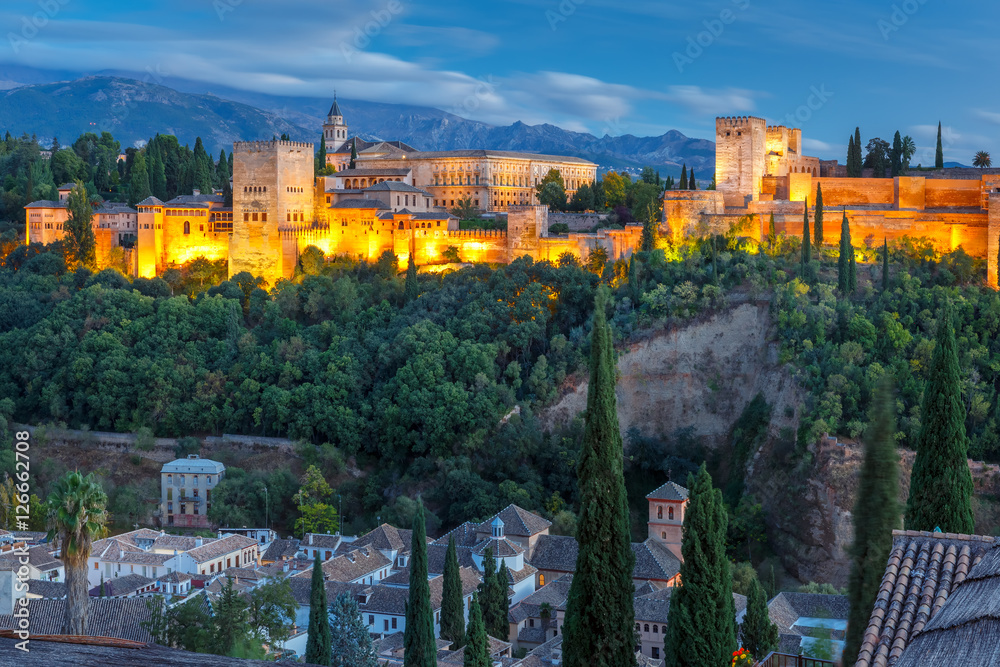 Moorish palace and fortress complex Alhambra with Comares Tower, Alcazaba, Palacios Nazaries and Palace of Charles V and roofs of Albayzin during evening blue hour in Granada, Andalusia, Spain