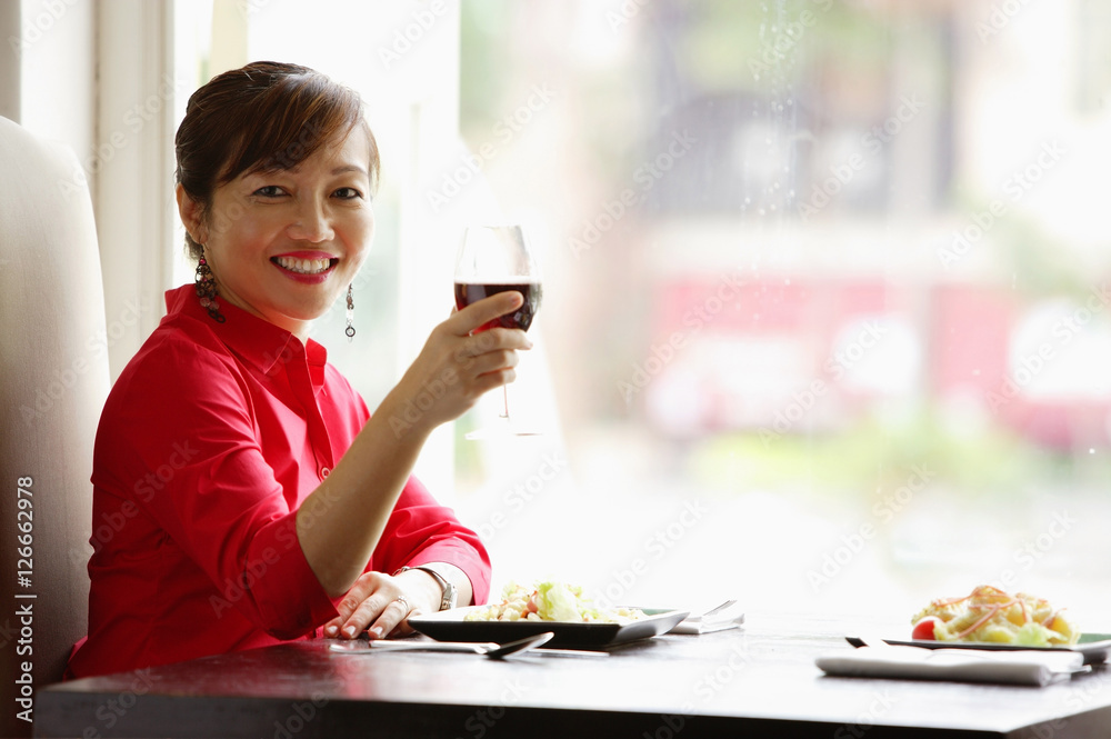 Woman sitting at table, raising drink towards camera, smiling Woman sitting at table, raising drink towards camera, smiling