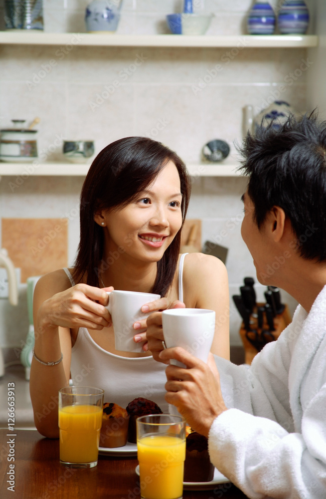 Couple in kitchen, having breakfast, both holding mugs Couple in kitchen, having breakfast, both holding mugs