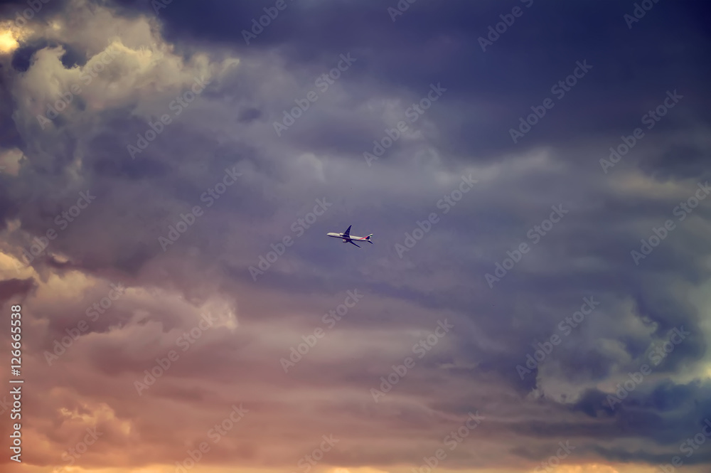The airplane passenger jet fly right in to the dark clouds just before storm. Colorful sunset rays. Emergency concept. The airplane passenger jet fly right in to the dark clouds just before storm. Colorful sunset rays. Emergency concept.