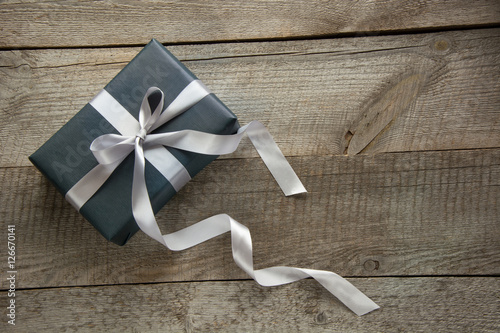 Gift box wrapped in black paper with silver ribbon on wooden surface. photo