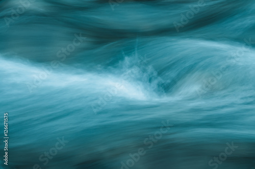 Abstract image of fast running water waves. The blue water waves and white splashes form unique abstract lines.