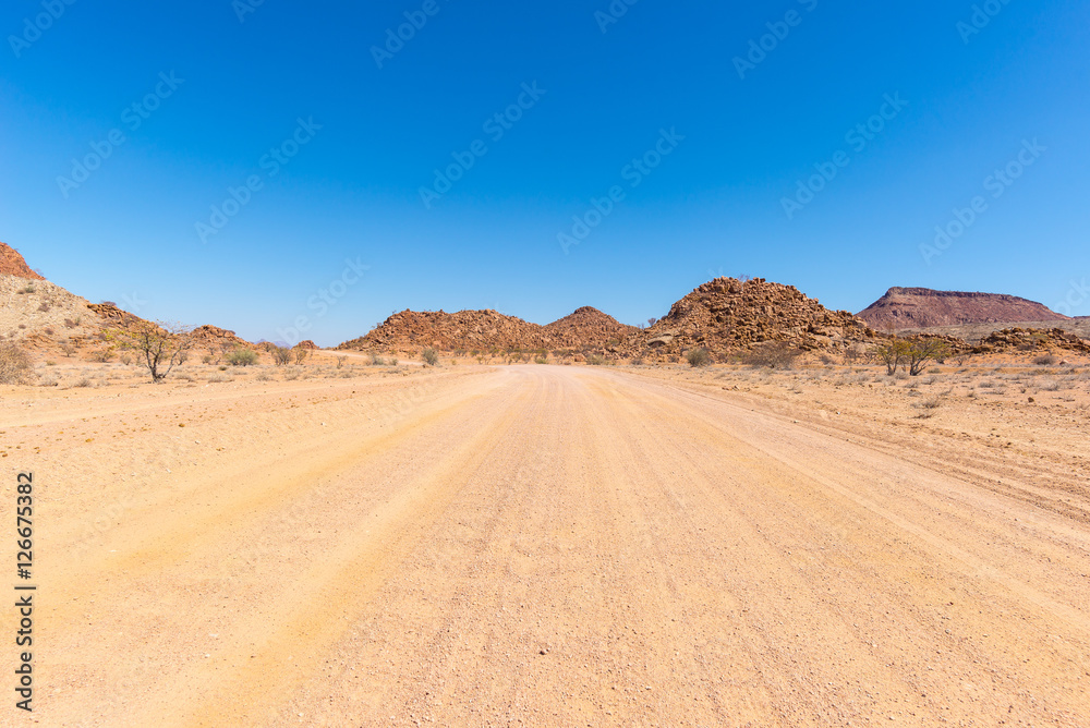 Gravel 4x4 road crossing the colorful desert at Twyfelfontein, in the majestic Damaraland Brandberg, scenic travel destination in Namibia, Africa.