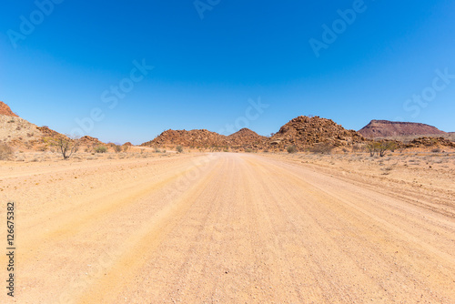 Gravel 4x4 road crossing the colorful desert at Twyfelfontein, in the majestic Damaraland Brandberg, scenic travel destination in Namibia, Africa. © fabio lamanna