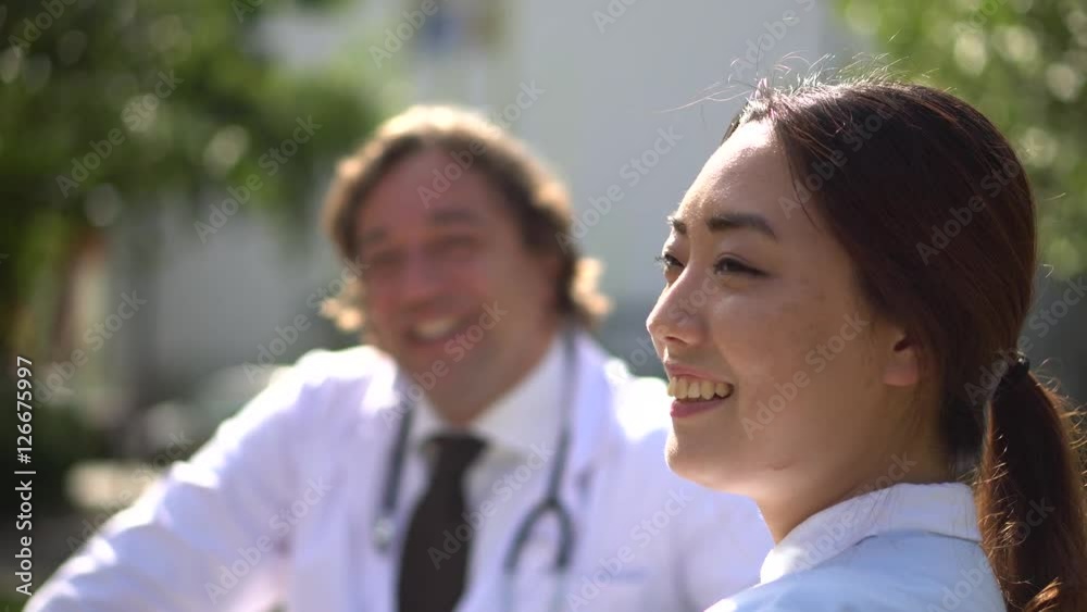 Profiled smiling Asian nurse talking outdoors with a male doctor Profiled smiling Asian nurse talking outdoors with a male doctor