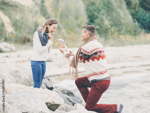 Photos Young attractive couple in knitted sweaters on a cliff on sea shore, man jokingl