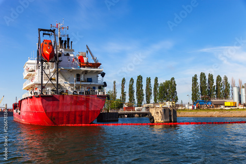 Cargo ship moored on port surrounded by oil spill barrier. photo