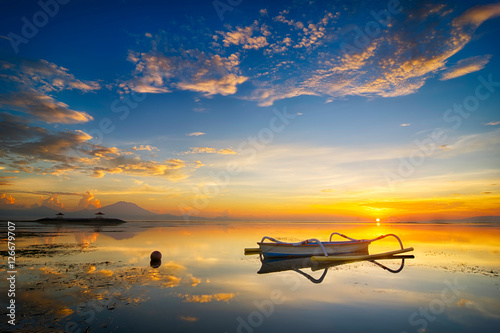 Beautiful seascape sunrise scenery with golden sun at horizon and fisherman boat as foreground at Bali, Indonesia