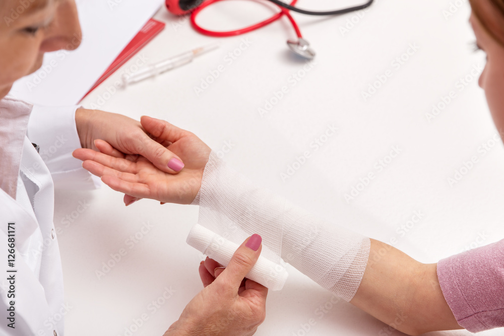 Ärztin legt Verband an, Frau mit verletztem Unterarm Ärztin legt Verband an, Frau mit verletztem Unterarm