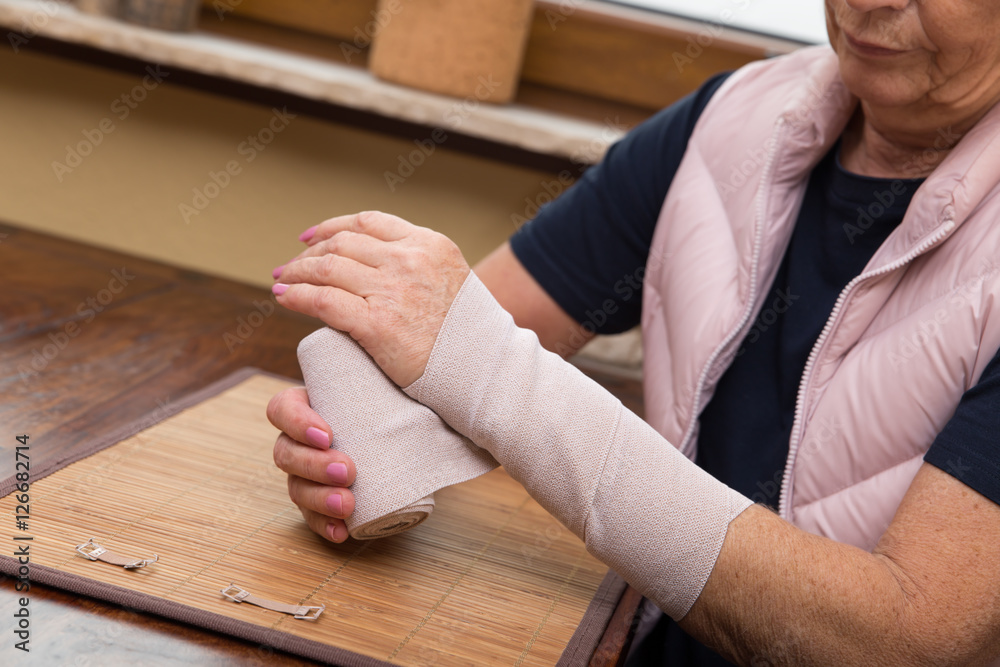 Ältere Frau verbindet sich ihren Arm mit einem Verband selbst Ältere Frau verbindet sich ihren Arm mit einem Verband selbst