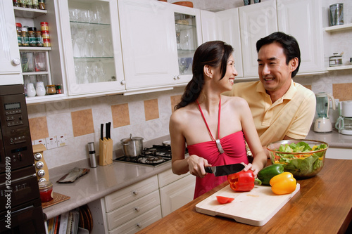 Couple in kitchen  woman chopping vegetables  looking over shoulder to smile at man