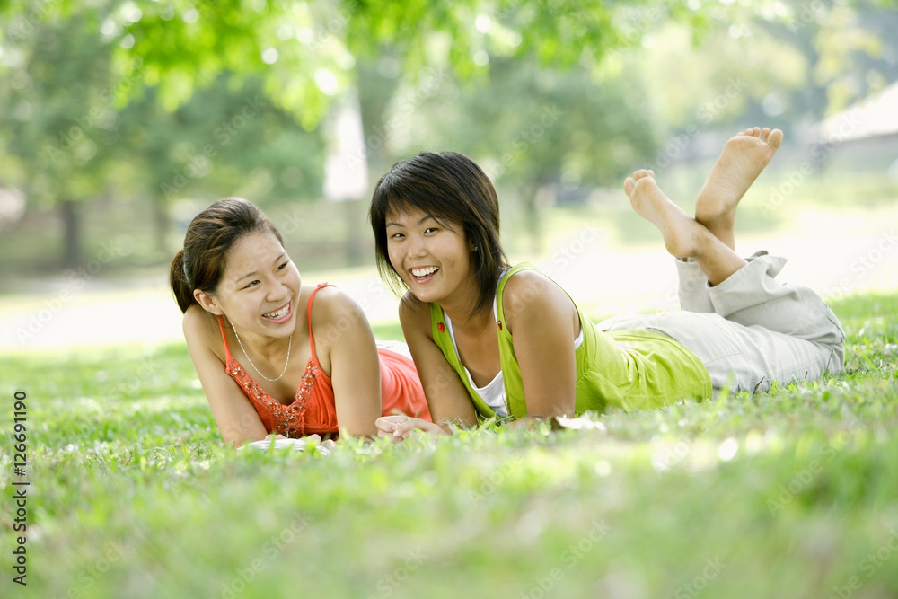 Two young women lying on grass, looking at camera