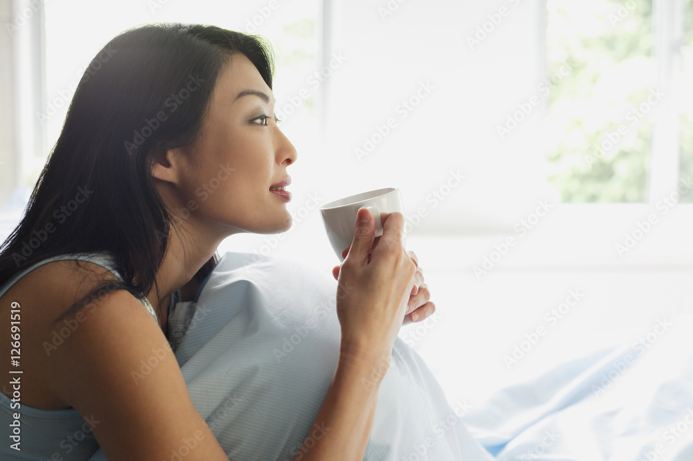 Woman sitting on bed, holding cup, looking away Woman sitting on bed, holding cup, looking away
