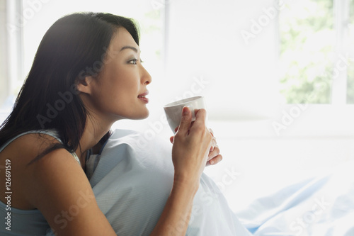 Woman sitting on bed, holding cup, looking away