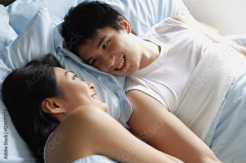 Couple in bed, looking at each other, smiling