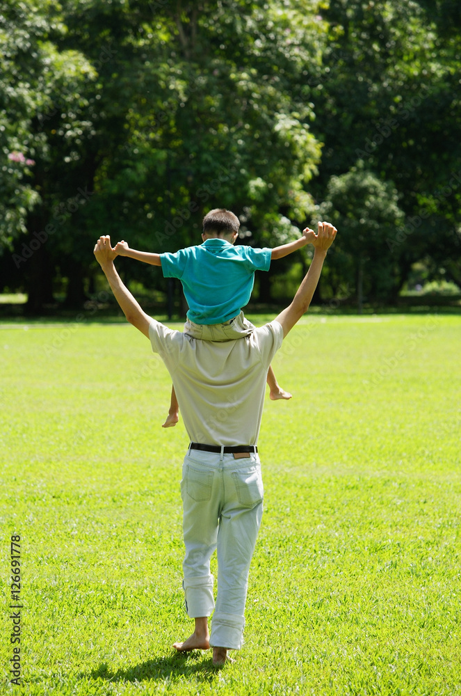 Father carrying son on shoulders, walking in field Father carrying son on shoulders, walking in field