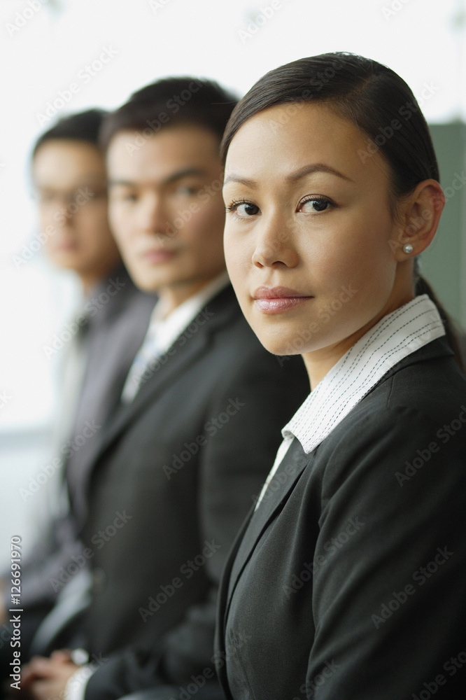 Business people seating in a row, looking at camera, focus on the woman Business people seating in a row, looking at camera, focus on the woman