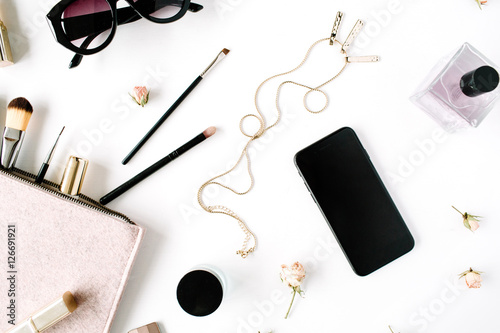 Flat lay, top view office table desk frame. feminine desk workspace with clutch, cosmetics, phone, sunglasses, lipstick rose buds on white background.