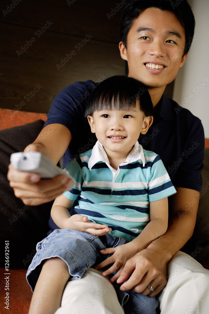 Father with young son on lap, holding TV remote control