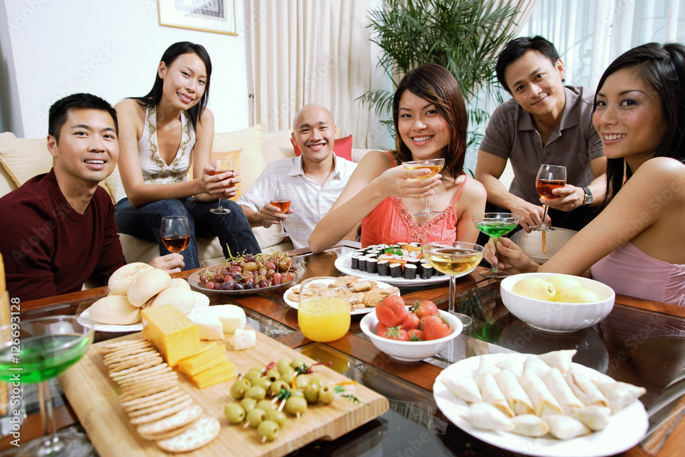 Adults having a party in living room, smiling at camera, food on coffee table